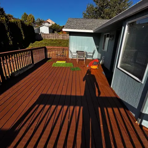 Freshly stained wood deck with railing beside a blue house